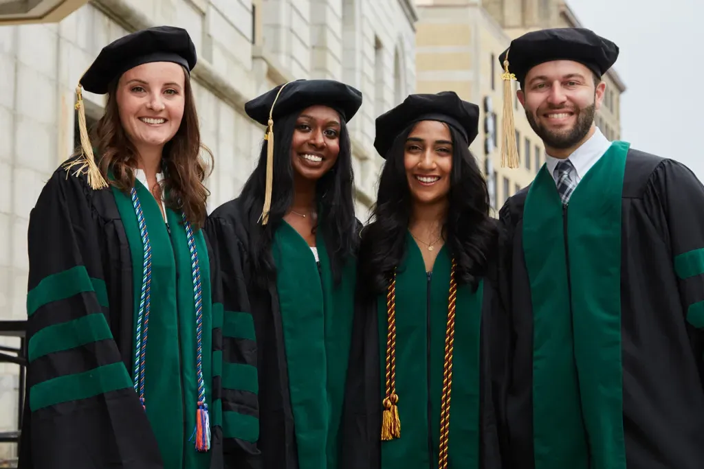 Four C O M students in their green and black academic regalia prior to their graduation ceremony